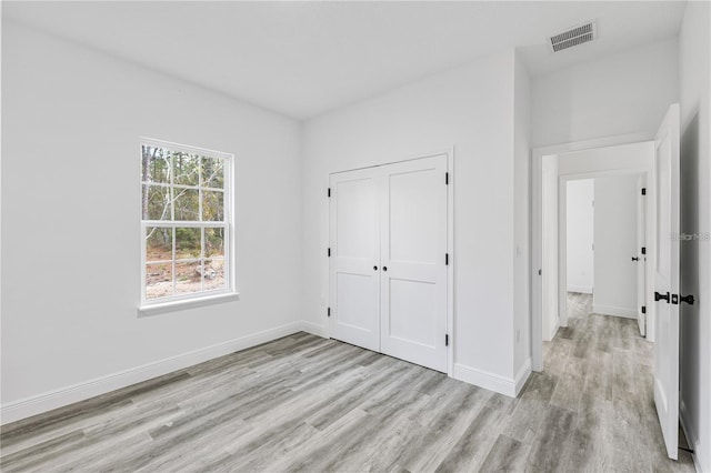 unfurnished bedroom featuring baseboards, visible vents, a closet, and light wood-style flooring