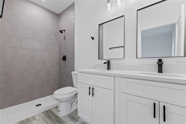 full bath featuring double vanity, toilet, tiled shower, and a sink