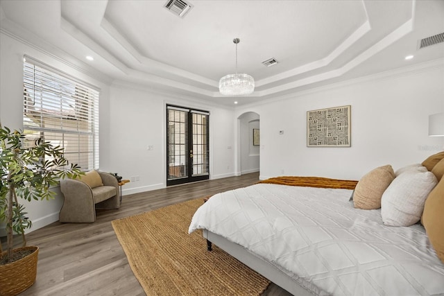 bedroom with arched walkways, a raised ceiling, light wood-style floors, ornamental molding, and recessed lighting