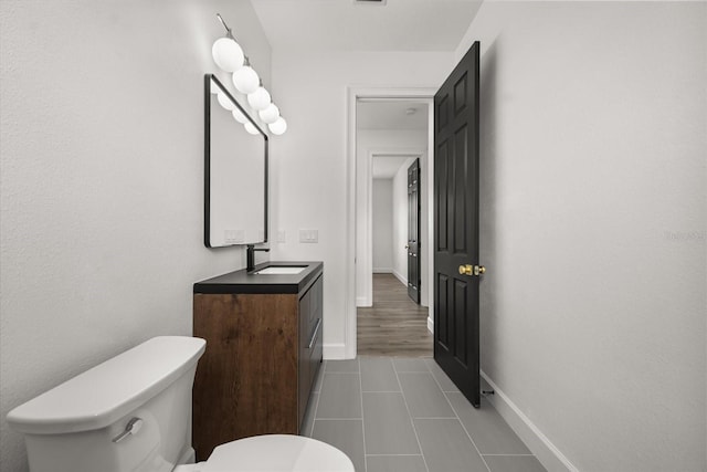half bathroom featuring tile patterned floors, toilet, vanity, and baseboards