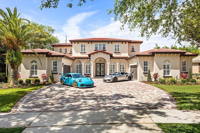 mediterranean / spanish-style house featuring an attached garage, french doors, decorative driveway, stucco siding, and a tiled roof