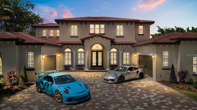 mediterranean / spanish-style home featuring an attached garage, french doors, decorative driveway, and stucco siding