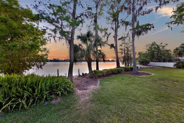 yard at dusk featuring a water view and fence