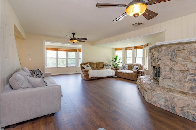 living area with dark wood-type flooring, visible vents, ceiling fan, and a stone fireplace