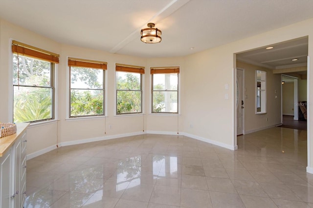 empty room with light tile patterned flooring, a healthy amount of sunlight, and baseboards