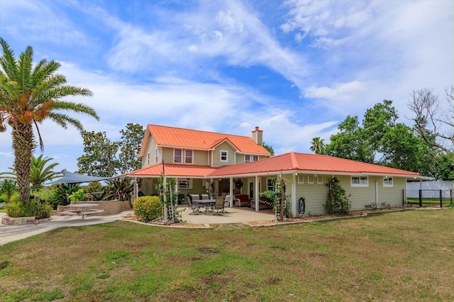 rear view of property with fence, a chimney, a patio area, metal roof, and a lawn