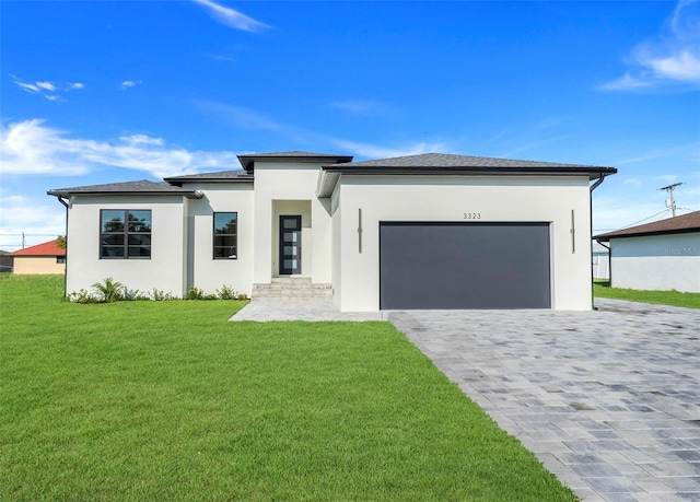 prairie-style house with stucco siding, decorative driveway, a front lawn, and an attached garage