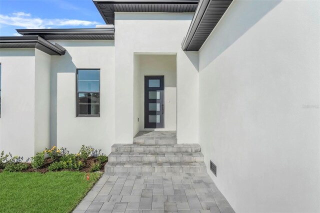 view of exterior entry with visible vents and stucco siding