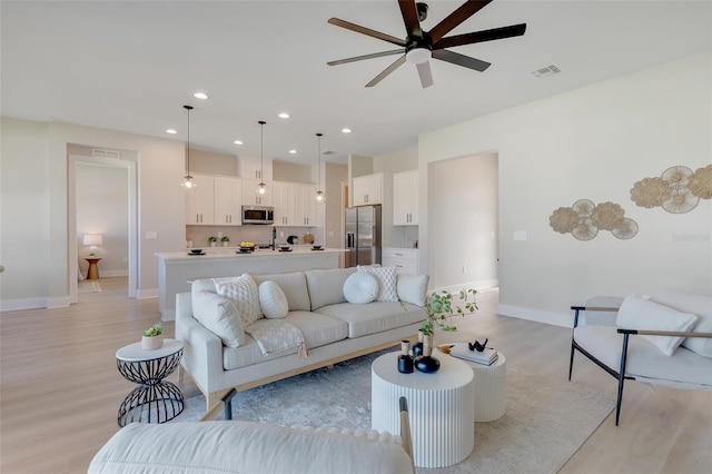 living room featuring baseboards, visible vents, ceiling fan, and light wood-style floors