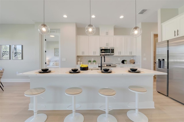 kitchen featuring decorative backsplash, appliances with stainless steel finishes, white cabinets, visible vents, and a kitchen breakfast bar