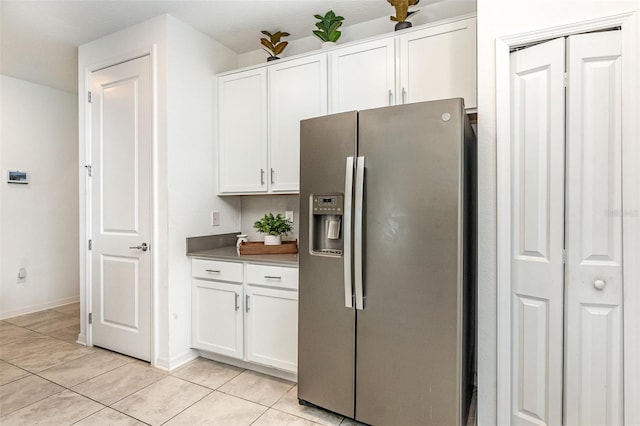 kitchen with light tile patterned floors, white cabinetry, baseboards, dark countertops, and stainless steel fridge with ice dispenser
