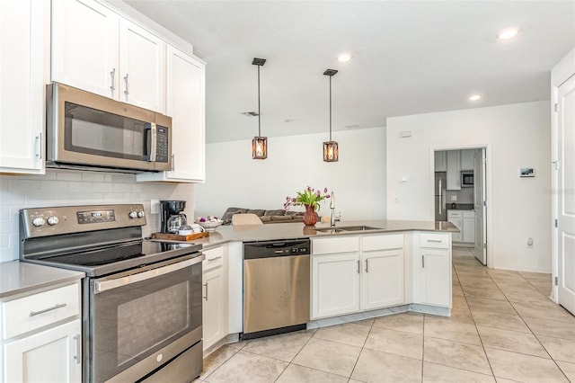 kitchen with tasteful backsplash, appliances with stainless steel finishes, white cabinets, a sink, and a peninsula