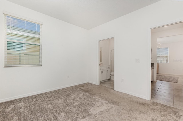 unfurnished bedroom featuring baseboards, light carpet, and ensuite bath