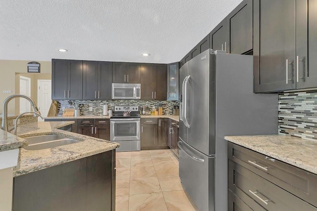 kitchen featuring a sink, light stone counters, stainless steel appliances, and decorative backsplash