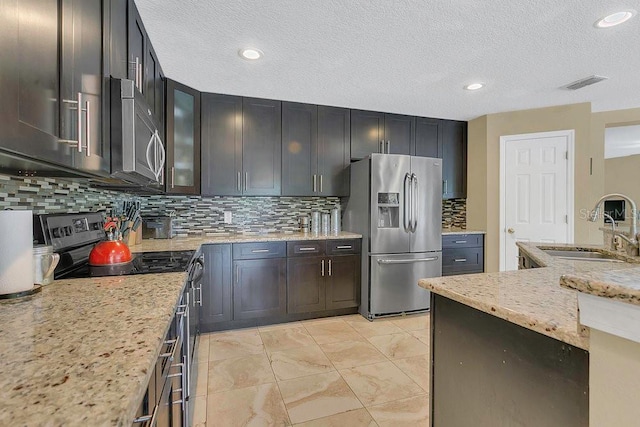 kitchen with decorative backsplash, a sink, appliances with stainless steel finishes, visible vents, and light stone countertops