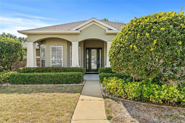property entrance featuring a yard, stucco siding, and roof with shingles