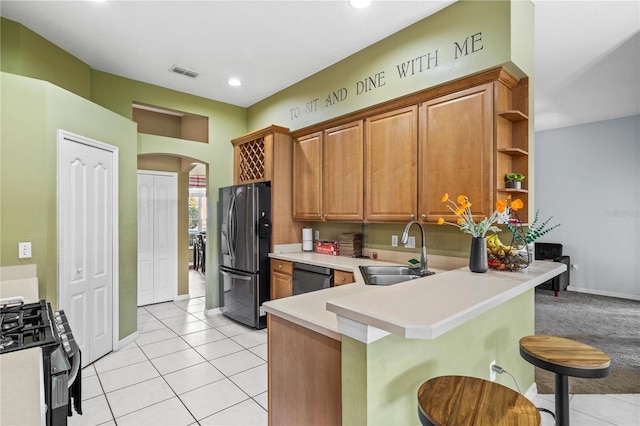 kitchen with a kitchen breakfast bar, black fridge with ice dispenser, a sink, gas range oven, and arched walkways