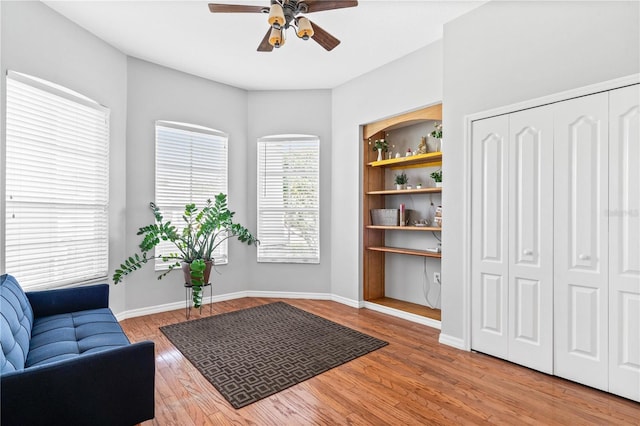 sitting room featuring wood finished floors, ceiling fan, built in features, and baseboards