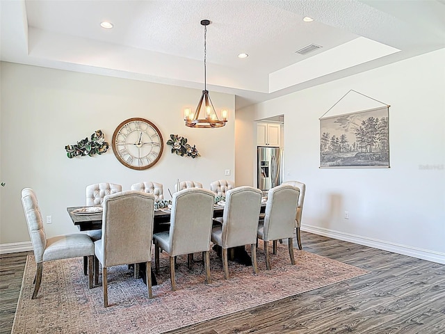 dining area featuring a raised ceiling, visible vents, dark wood-style floors, baseboards, and a notable chandelier