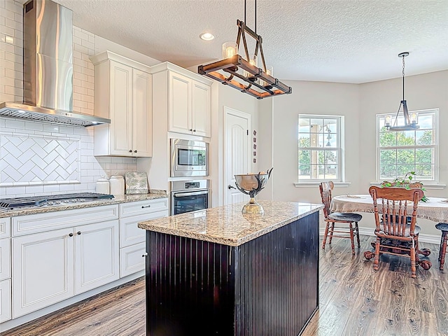 kitchen with wall chimney exhaust hood, a textured ceiling, appliances with stainless steel finishes, and wood finished floors