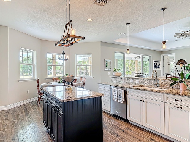 kitchen with wood finished floors, stainless steel dishwasher, a sink, visible vents, and a textured ceiling