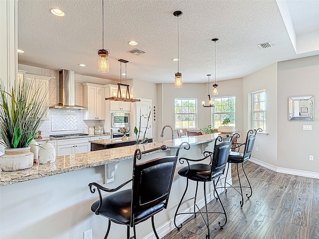 kitchen featuring appliances with stainless steel finishes, visible vents, light wood-style flooring, and wall chimney exhaust hood