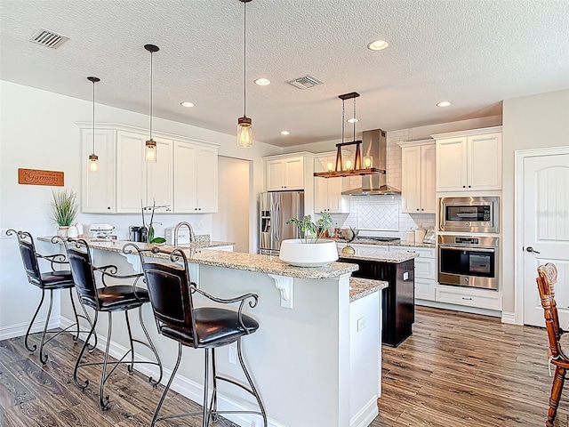 kitchen featuring visible vents, stainless steel appliances, a peninsula, and wall chimney range hood
