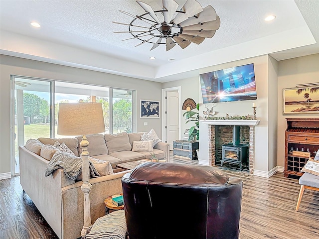 living room with a raised ceiling, wood finished floors, a wood stove, and baseboards