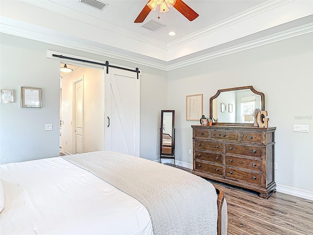 bedroom with wood finished floors, visible vents, a barn door, and baseboards
