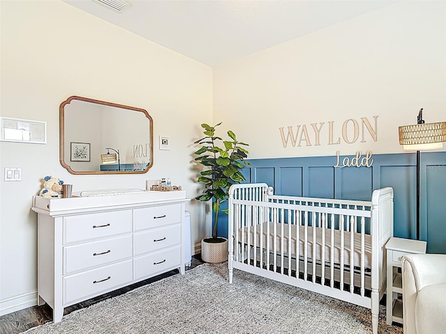 bedroom featuring baseboards, visible vents, a nursery area, and a wainscoted wall