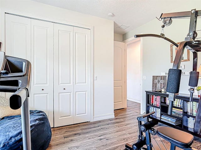 exercise area with a textured ceiling, visible vents, wood finished floors, and baseboards