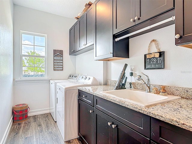 laundry room featuring a sink, baseboards, washer and dryer, cabinet space, and wood finished floors