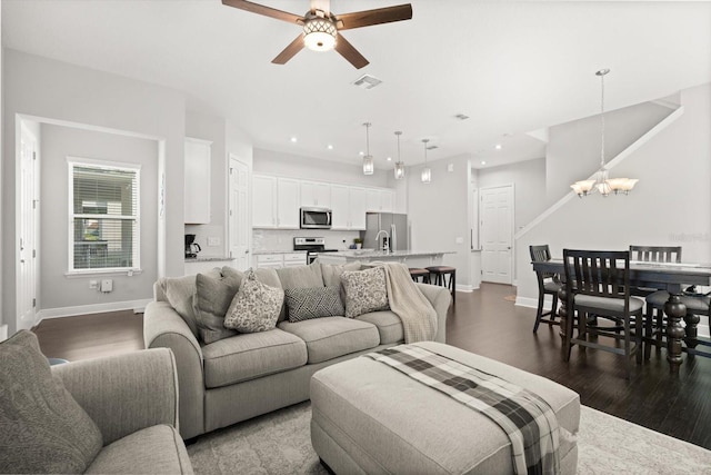 living area featuring a chandelier, a ceiling fan, dark wood-type flooring, baseboards, and recessed lighting