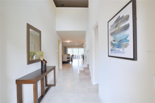 hallway featuring a towering ceiling, light tile patterned floors, stairs, and baseboards