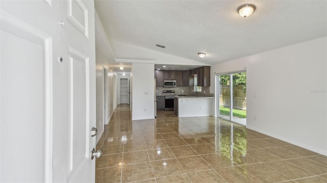 unfurnished living room with light tile patterned floors, vaulted ceiling, baseboards, visible vents, and a textured ceiling