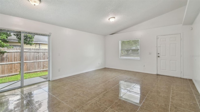 tiled spare room featuring a textured ceiling, lofted ceiling, and baseboards