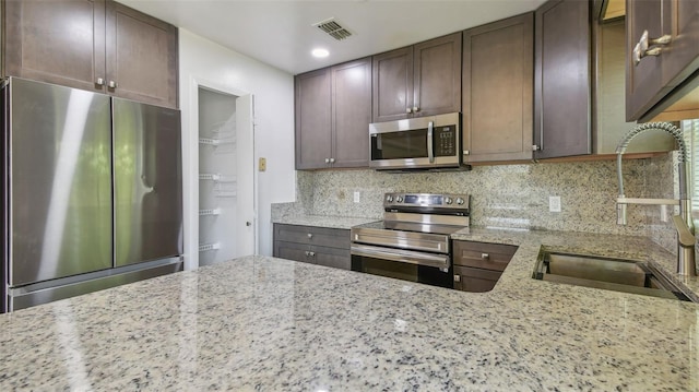 kitchen featuring light stone counters, stainless steel appliances, backsplash, a sink, and visible vents
