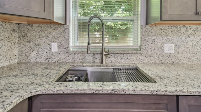 kitchen featuring a sink, light stone counters, and decorative backsplash