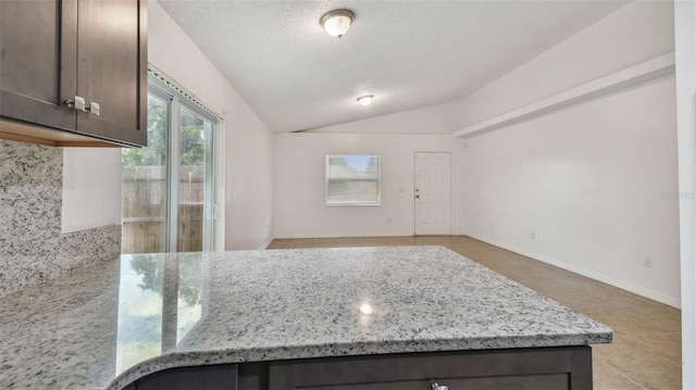 kitchen with light tile patterned floors, dark brown cabinetry, light stone countertops, and vaulted ceiling