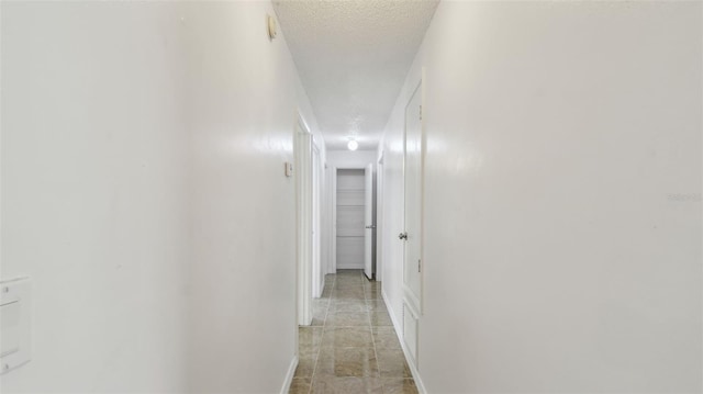 corridor featuring baseboards, light tile patterned floors, and a textured ceiling