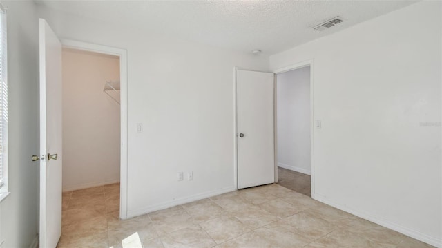 unfurnished bedroom featuring visible vents, a spacious closet, a textured ceiling, and a closet