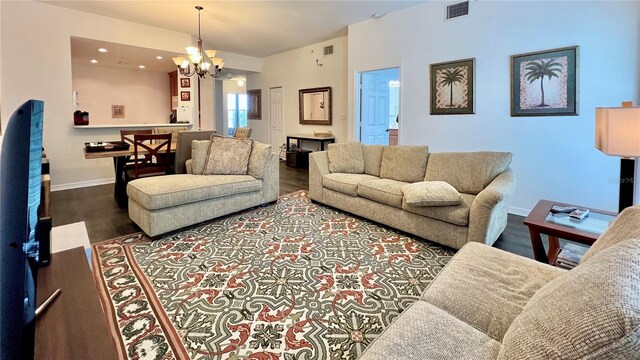 living room featuring a notable chandelier, visible vents, baseboards, and wood finished floors