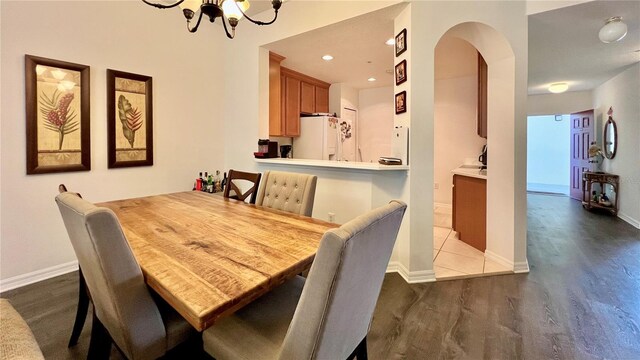 dining space featuring arched walkways, baseboards, a chandelier, and wood finished floors