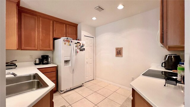 kitchen with brown cabinetry, light tile patterned flooring, light countertops, a sink, and white fridge with ice dispenser