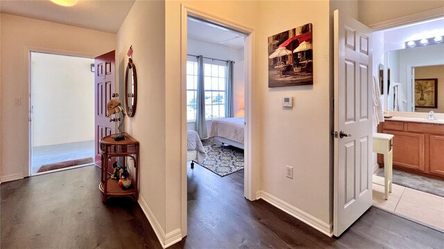 hall featuring a sink, baseboards, and dark wood-type flooring