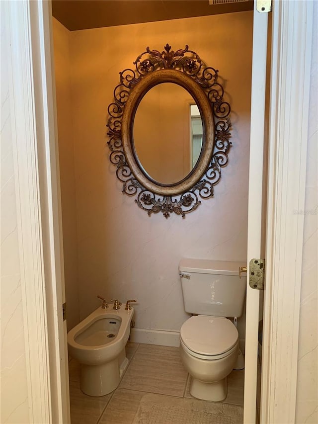 half bath with baseboards, a bidet, toilet, and tile patterned flooring