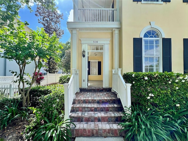 entrance to property featuring a balcony, stucco siding, and fence