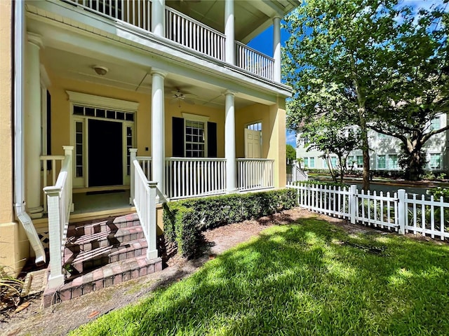 view of exterior entry featuring a lawn, a balcony, covered porch, and fence