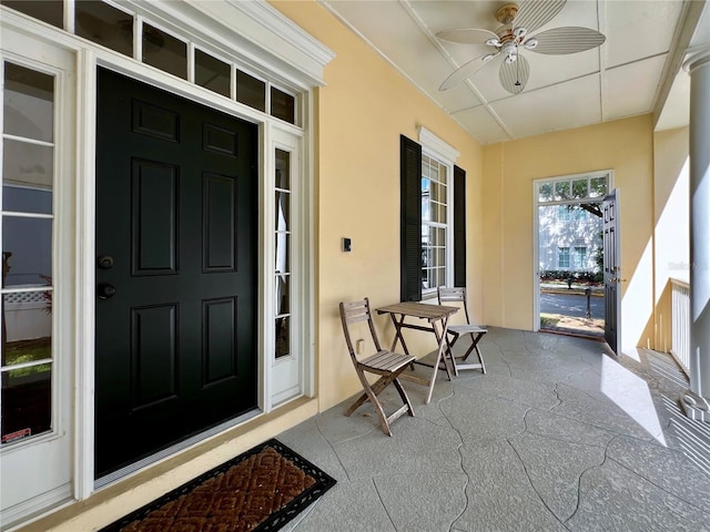 view of exterior entry with a porch, ceiling fan, and stucco siding