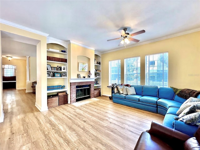 living area with ceiling fan, light wood finished floors, a brick fireplace, baseboards, and crown molding